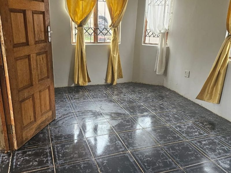 An empty bedroom featuring dark tiled flooring, a solid wooden door, and windows fitted with security bars.