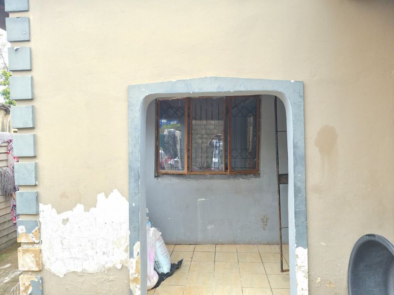A small covered patio area featuring tiled flooring and an arched entrance, currently showing signs of exterior wall paint deterioration.