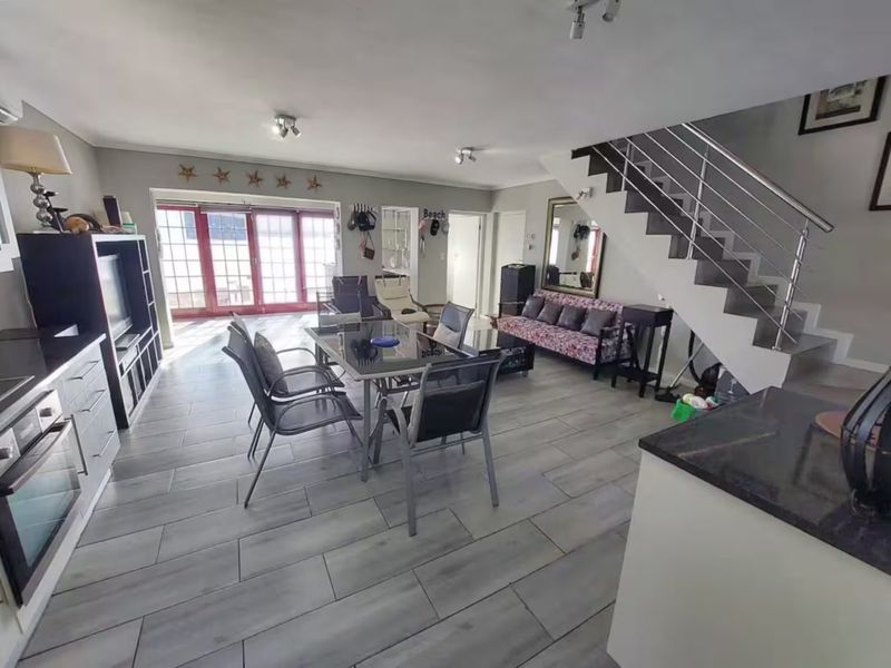 Spacious open-plan living and dining area featuring modern tiled flooring, a sleek staircase with stainless steel balustrades, and direct access to the outdoors.