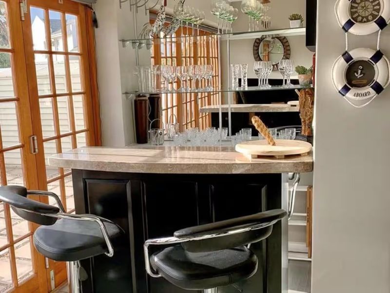A dedicated home bar area featuring a built-in counter with a stone top, mirrored backsplash, glass shelving, and direct access to the outdoors via french doors.