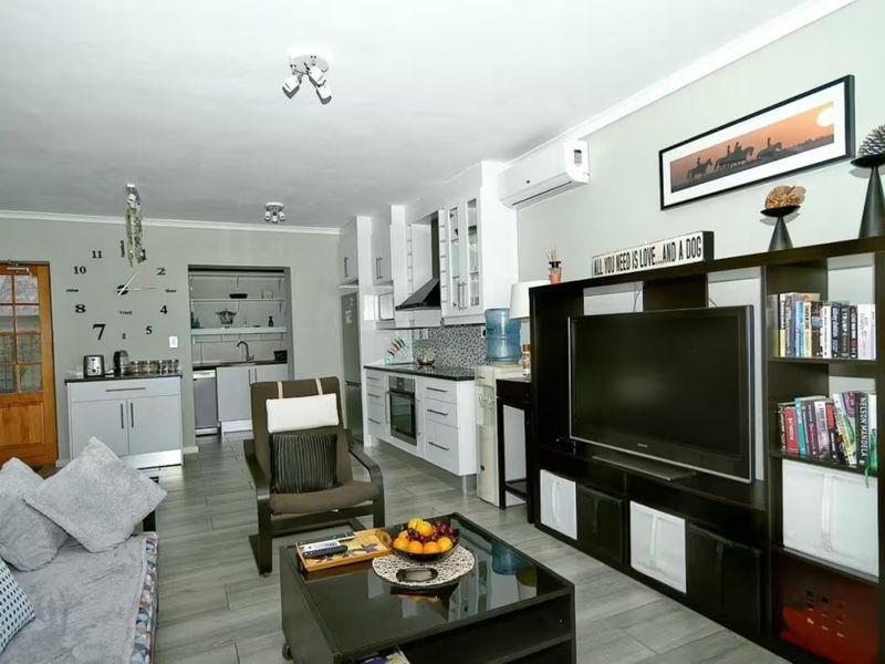 Open-plan living area featuring a modern kitchen with built-in cabinetry, integrated appliances, and a separate scullery, complemented by tiled flooring and air conditioning.