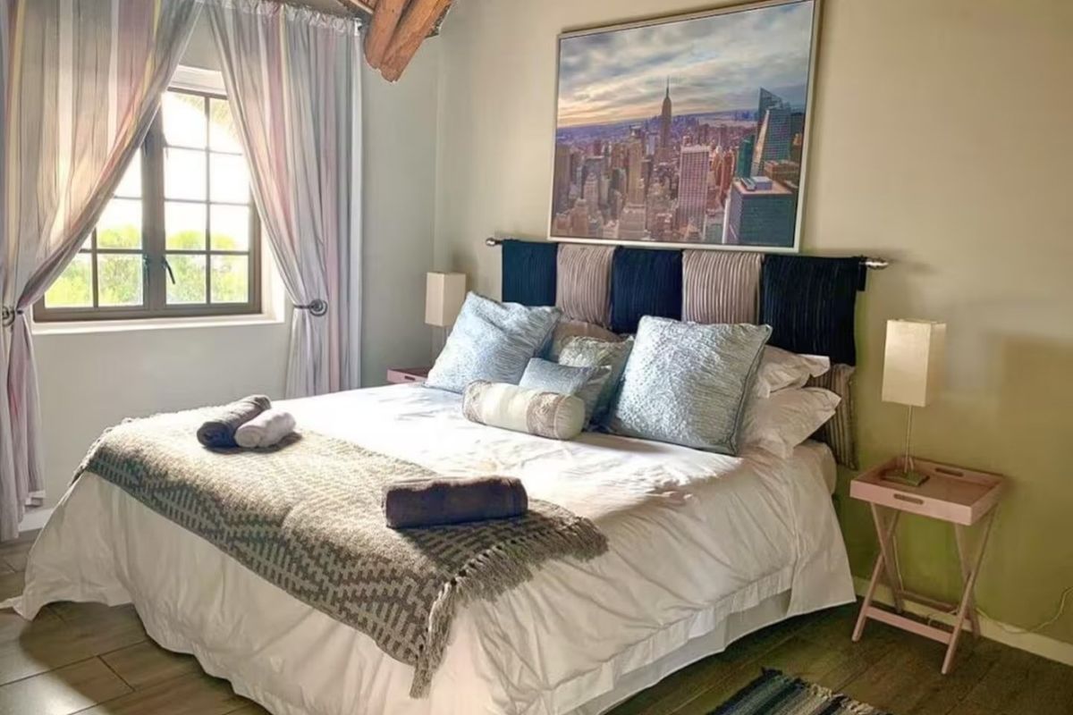 A cozy bedroom featuring exposed timber rafters, tiled flooring, and a window with natural light.