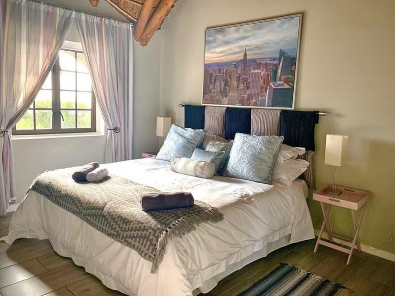 A cozy bedroom featuring exposed timber rafters, tiled flooring, and a window with natural light.