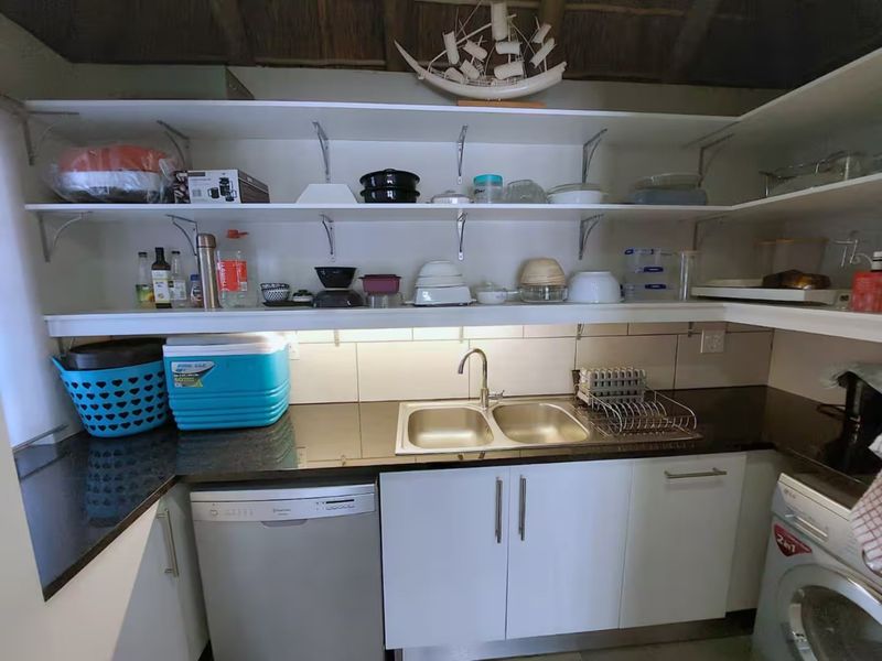 A functional scullery featuring granite countertops, a double bowl sink, open shelving, and integrated space for a dishwasher and washing machine.
