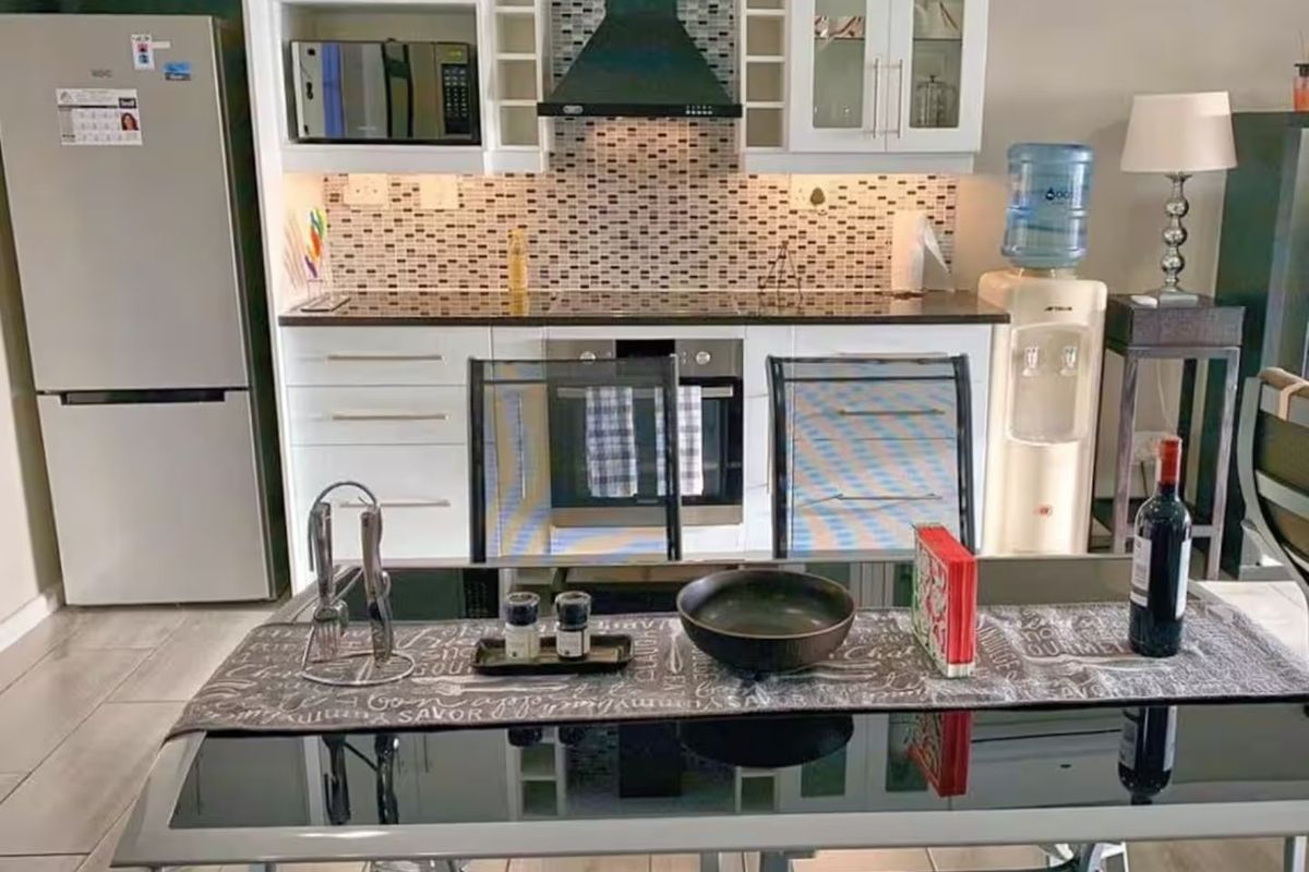 A functional kitchen featuring white cabinetry, a mosaic tile backsplash, built-in oven, extractor fan, and integrated microwave, complemented by tiled flooring.