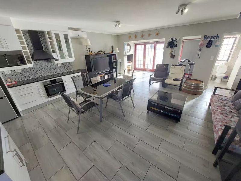 Spacious open-plan living area featuring a modern kitchen with mosaic backsplash, tiled flooring, and direct access to the outdoor patio through glass sliding doors.