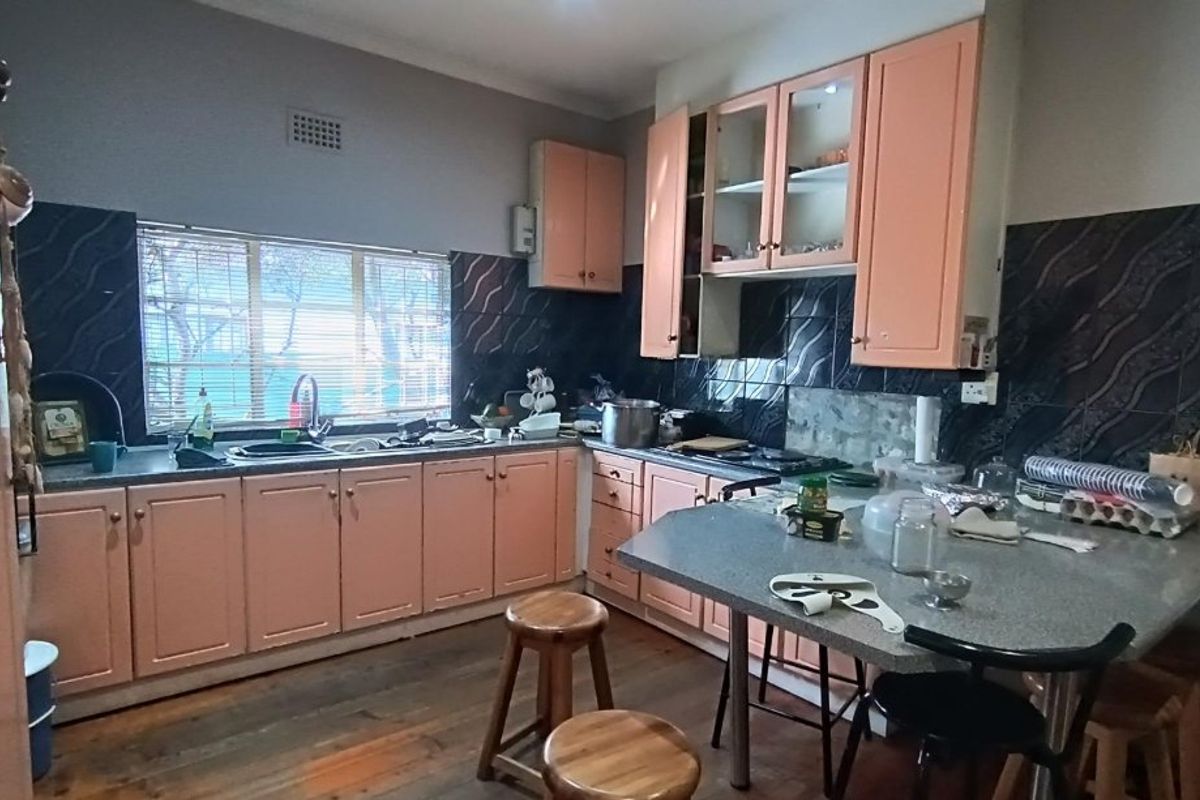 A functional kitchen featuring built-in cabinetry, laminate countertops, a double sink, and a tiled splashback, with timber flooring throughout.