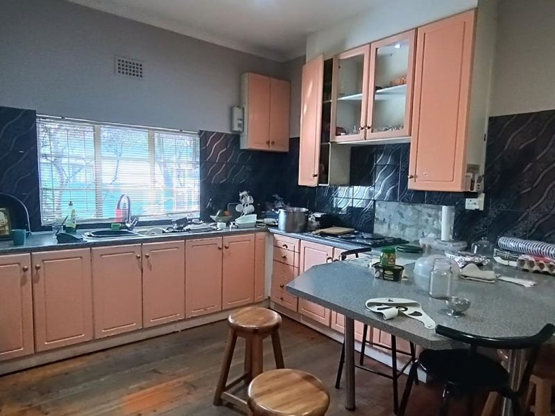 A functional kitchen featuring built-in cabinetry, laminate countertops, a double sink, and a tiled splashback, with timber flooring throughout.