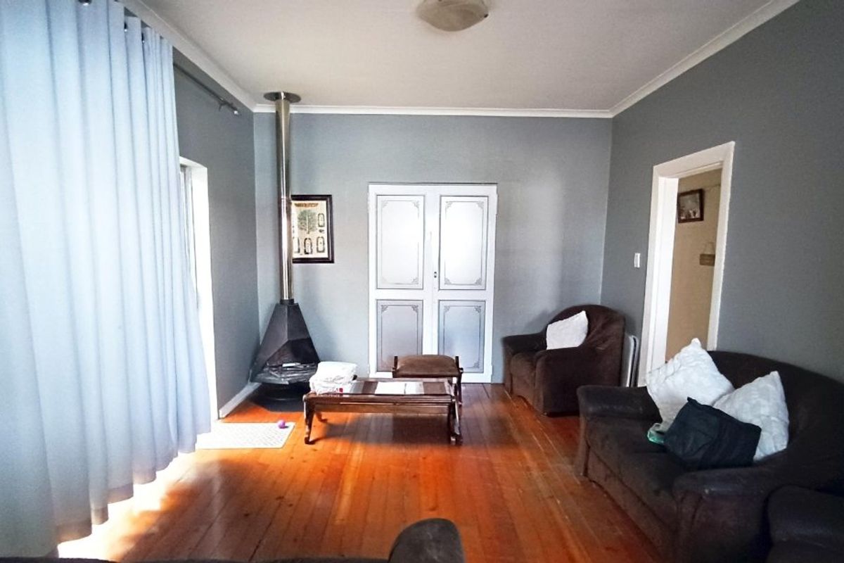 A living room featuring polished hardwood flooring, a freestanding fireplace, and built-in storage cupboards.