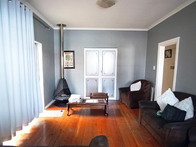 A living room featuring polished hardwood flooring, a freestanding fireplace, and built-in storage cupboards.