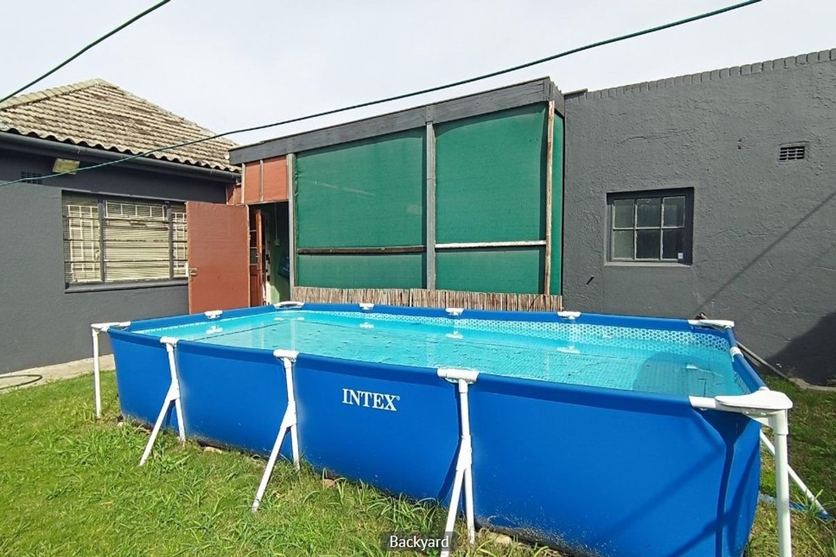Rear exterior view of the property featuring a grassed backyard area and painted masonry walls.