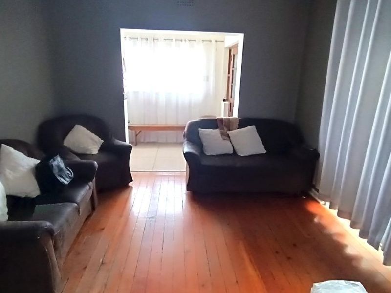 A living room featuring original hardwood flooring and a large opening leading to an adjacent space, providing a functional layout with natural light.