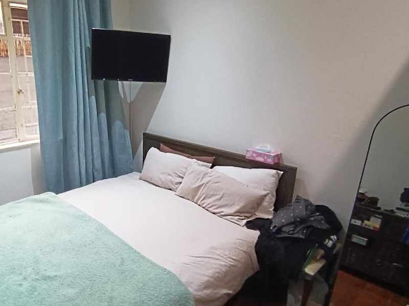 A standard bedroom featuring a window with security bars, providing natural light and basic ventilation.