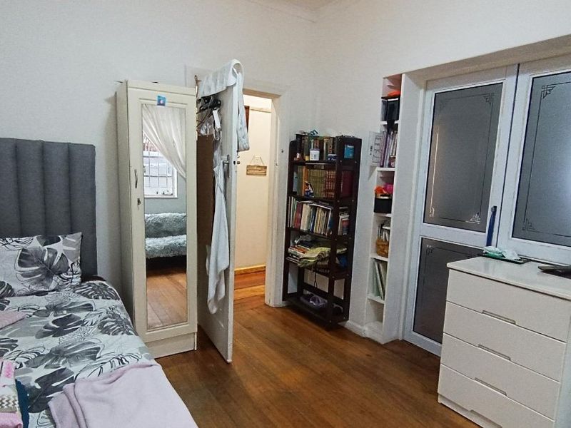 A bedroom featuring hardwood flooring, built-in shelving units, and a frosted glass door leading to an adjacent space.