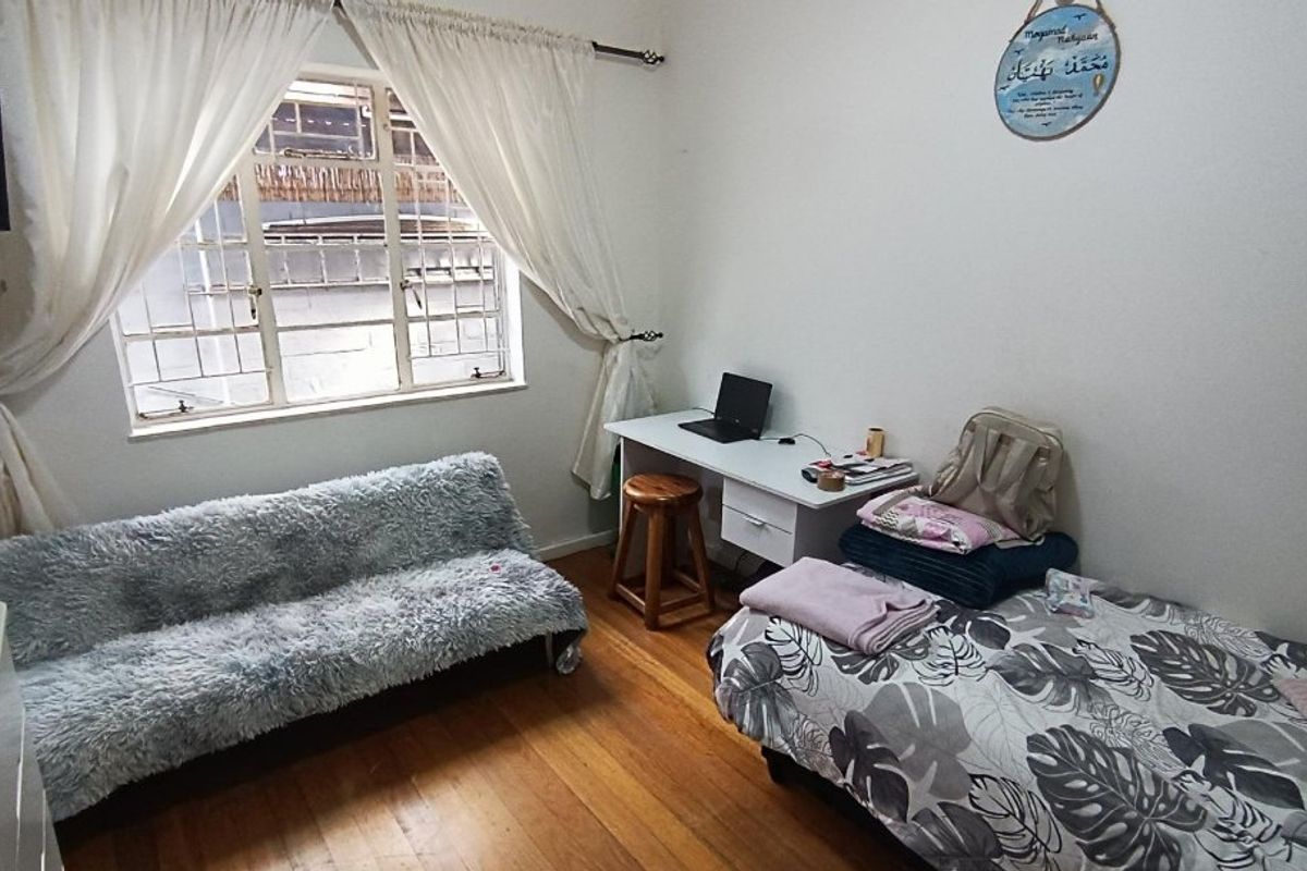 A bedroom featuring hardwood flooring and a window fitted with security bars, providing natural light and a functional layout.