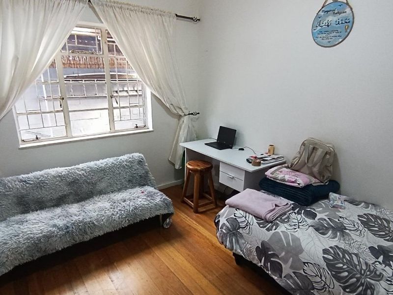 A bedroom featuring hardwood flooring and a window fitted with security bars, providing natural light and a functional layout.