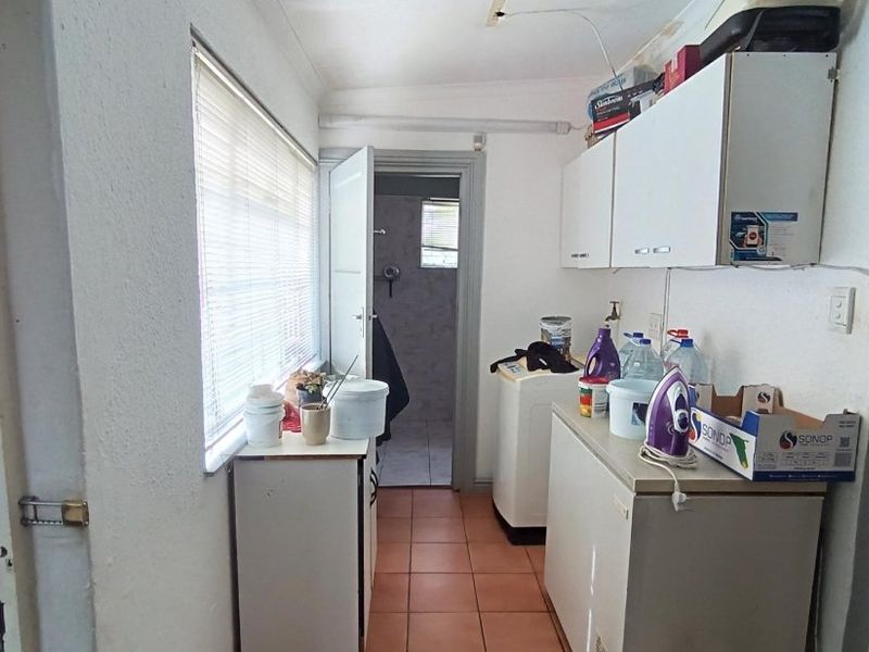 A functional laundry area featuring built-in cabinetry, tiled flooring, and direct access to an adjacent bathroom space.