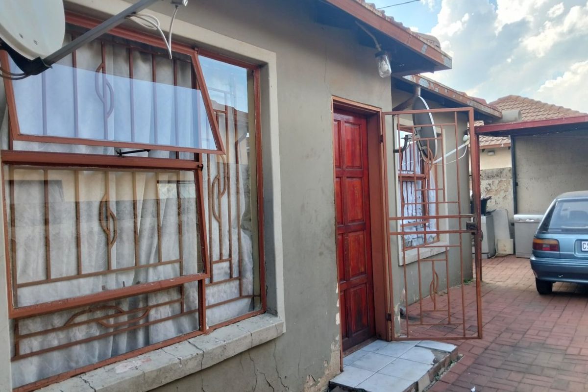 Rear exterior view of the property featuring a paved courtyard, security gates, and window bars with visible wear to the exterior wall plaster.
