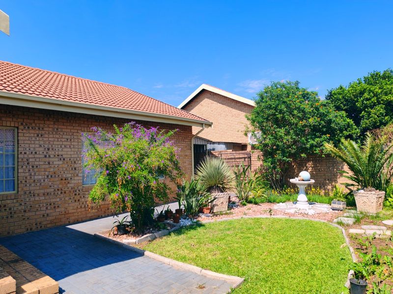 A well-maintained rear garden featuring a paved patio area, established landscaping, and a brick-built house exterior with a tiled roof.