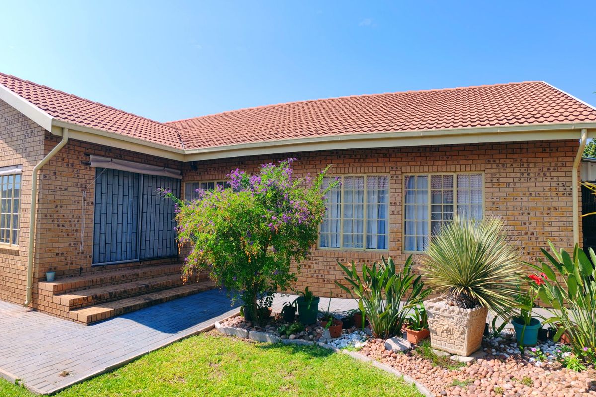 A well-maintained rear exterior view of a face brick house featuring a tiled roof, paved patio area, and established garden landscaping.