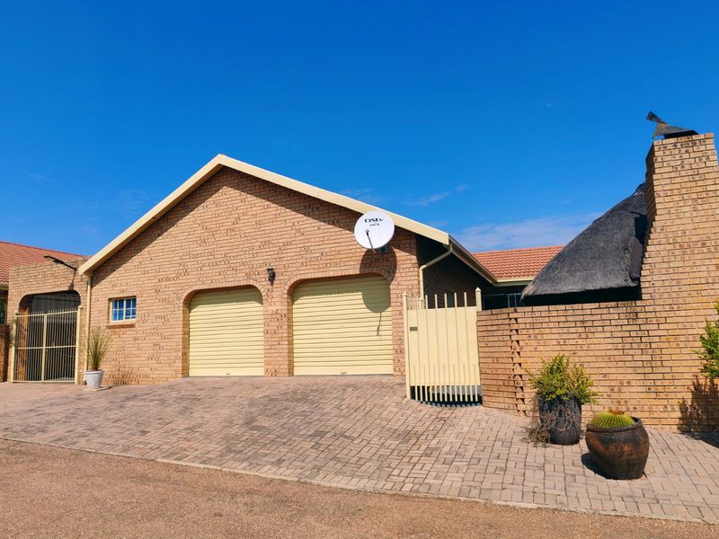 Front exterior view of a brick house featuring a double garage, paved driveway, and a section with a traditional thatched roof.