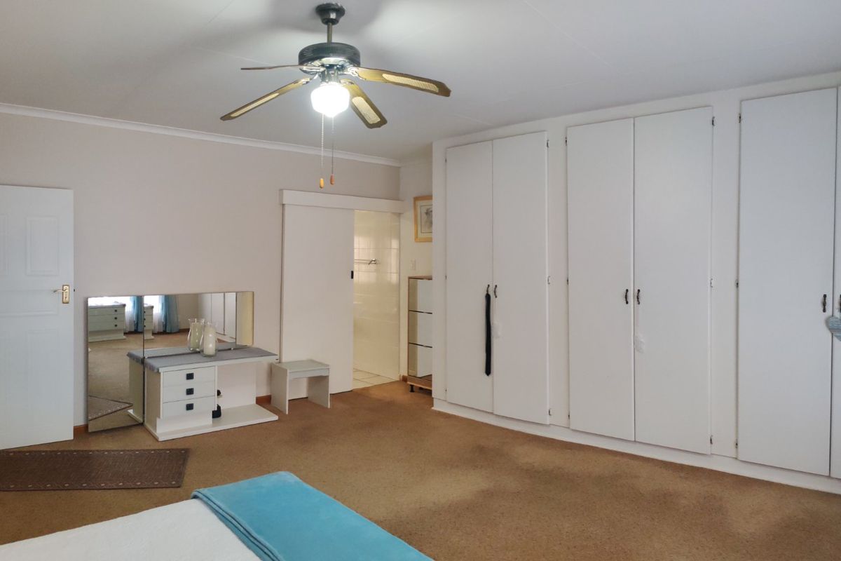 Spacious bedroom featuring neutral walls, carpeted flooring, a ceiling fan, and extensive built-in cupboard storage with an adjoining en-suite bathroom.
