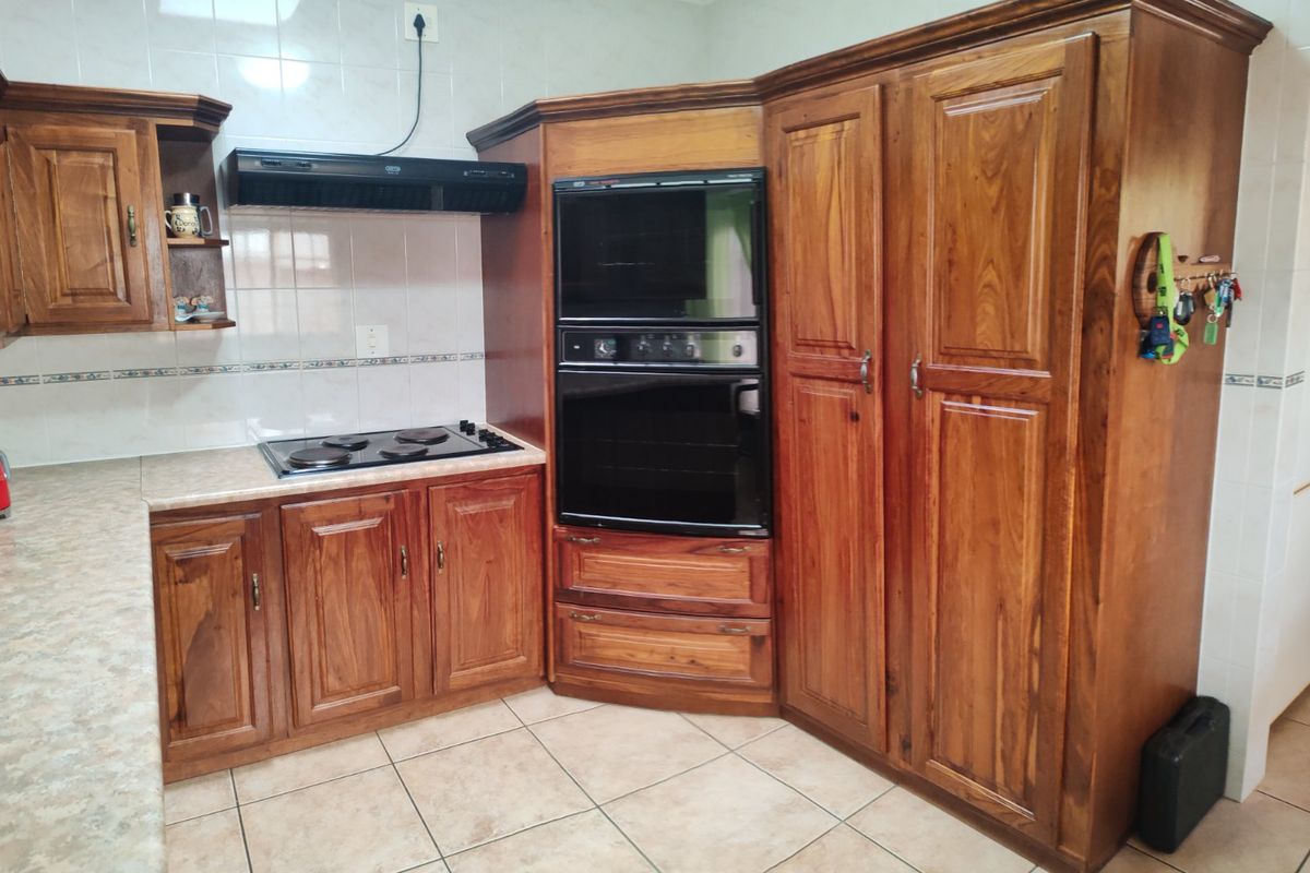 A functional kitchen featuring traditional wooden cabinetry, built-in oven, electric hob, extractor fan, and tiled splashback with neutral floor tiles.