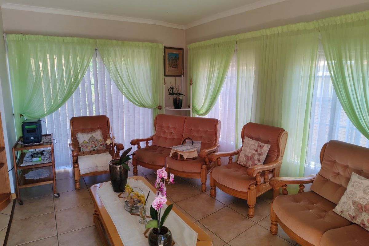 A living room featuring tiled flooring and a built-in shelving unit, illuminated by natural light through large windows with light green curtains.