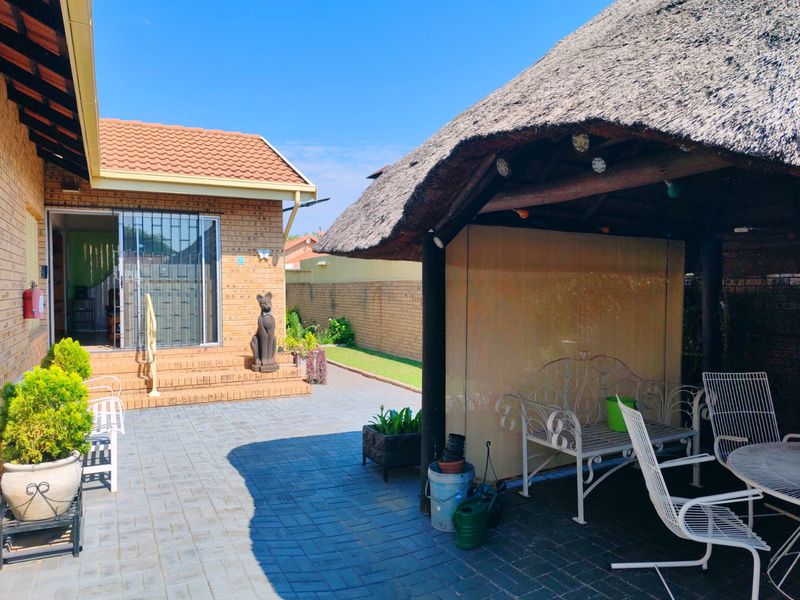 A covered outdoor patio area featuring a traditional thatched roof structure, brick paving, and direct access to the main house through a sliding door.