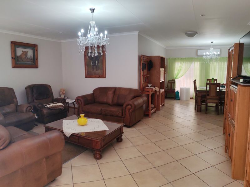 Spacious open-plan living and dining area featuring ceramic floor tiles, decorative chandeliers, and a wall-mounted air conditioning unit.