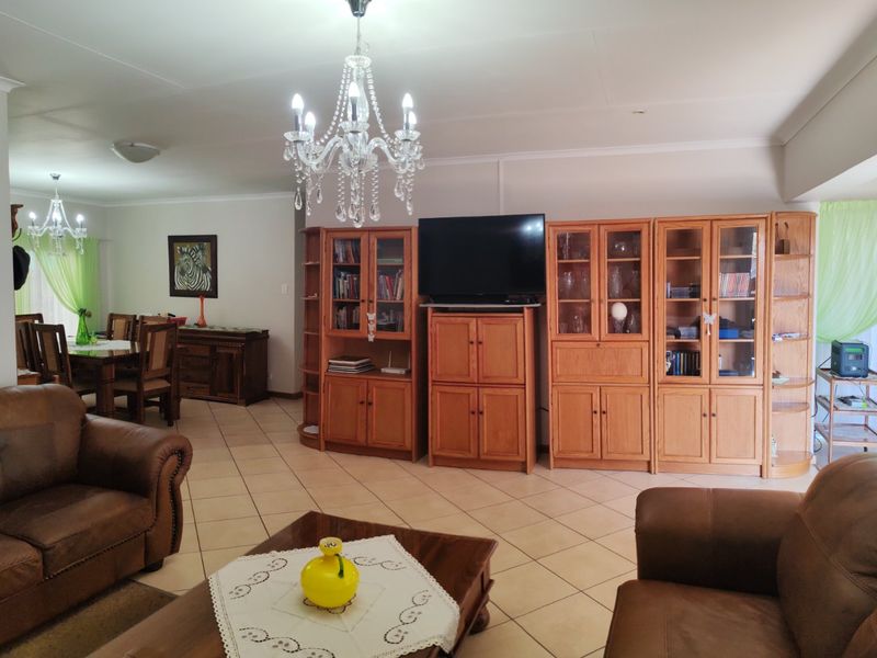 Spacious open-plan living and dining area featuring ceramic floor tiles, decorative chandeliers, and neutral wall finishes.