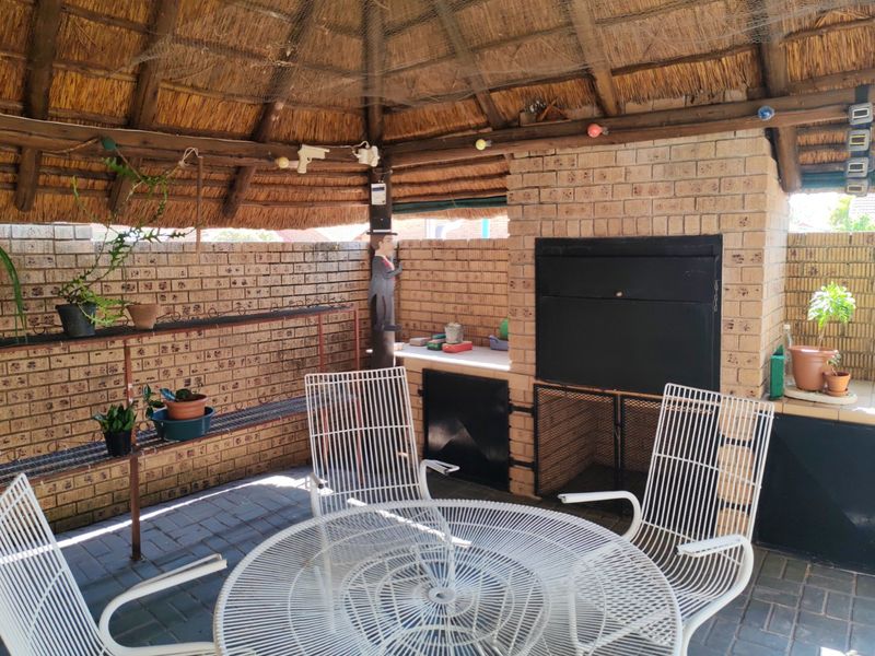 Covered outdoor patio area featuring a traditional thatch roof, built-in brick braai, and paved flooring, ideal for outdoor entertaining.