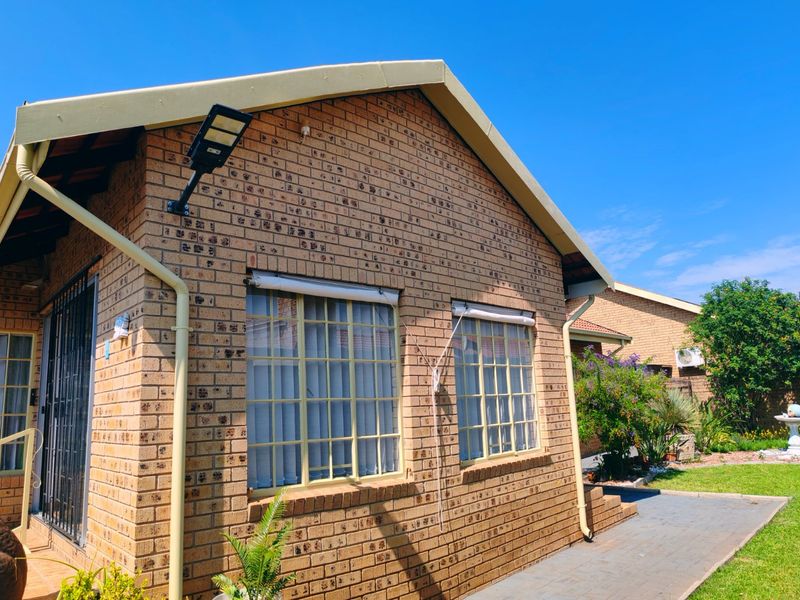 Rear view of the property featuring a face brick facade, security lighting, and a paved walkway leading to the garden area.