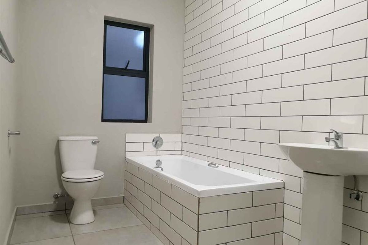 A clean, modern bathroom featuring a built-in bathtub with subway tile surround, a pedestal basin, and a toilet.