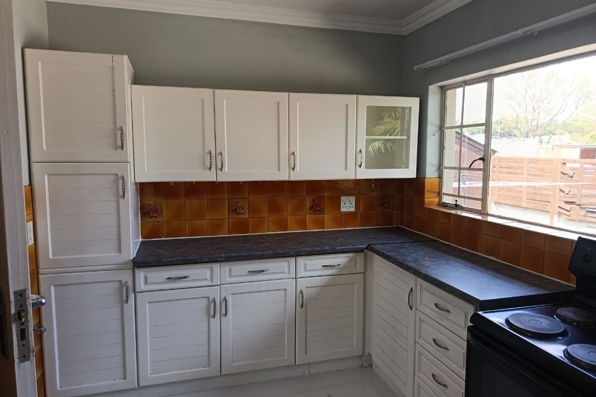 A functional kitchen featuring white built-in cabinetry, dark laminate countertops, and a classic tiled backsplash with natural light from the window.