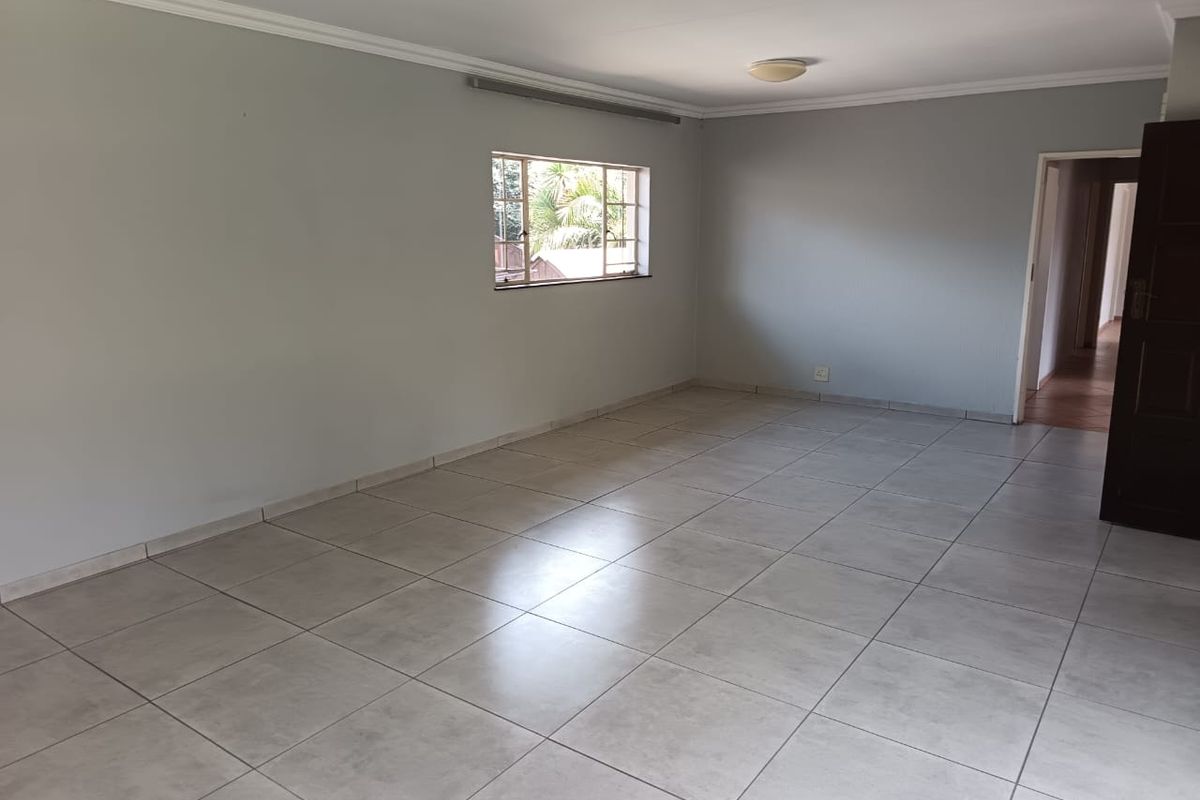 A spacious, empty living area featuring neutral tiled flooring, clean walls, and classic cornicing, offering a versatile blank canvas for interior design.