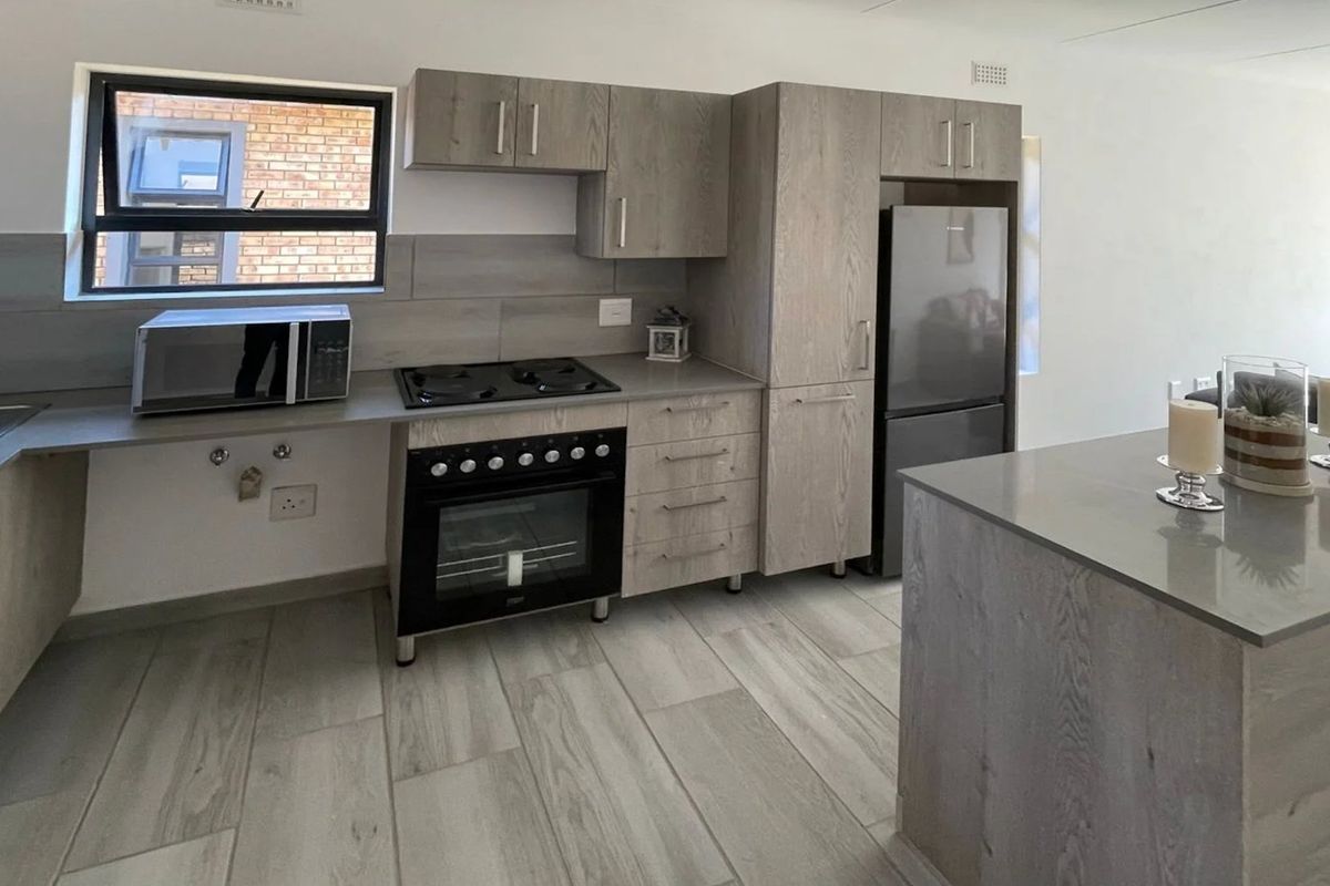 Modern kitchen featuring light wood-grain cabinetry, stone countertops, built-in oven, gas hob, and tiled flooring in an open-plan layout.