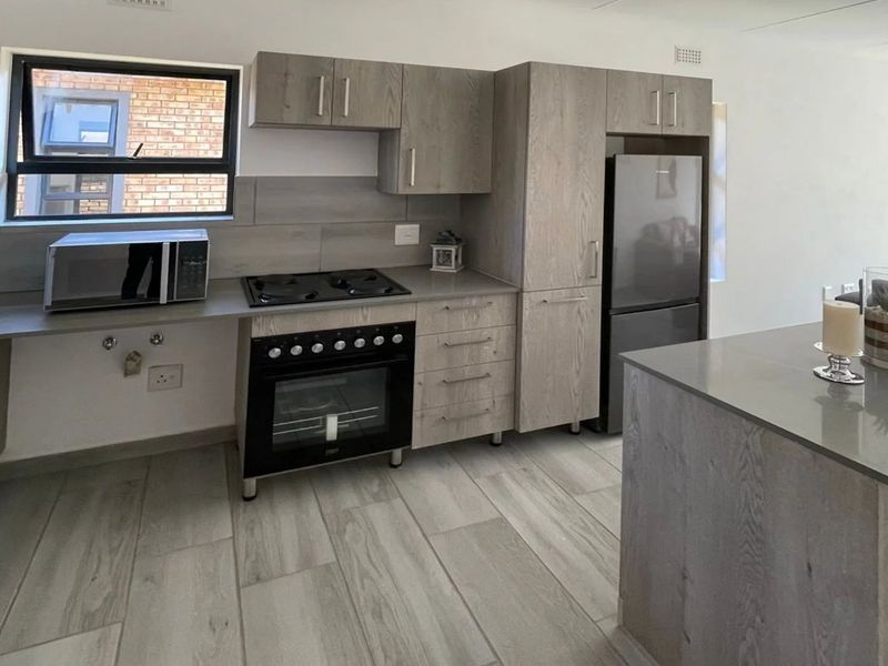 Modern kitchen featuring light wood-grain cabinetry, stone countertops, built-in oven, gas hob, and tiled flooring in an open-plan layout.