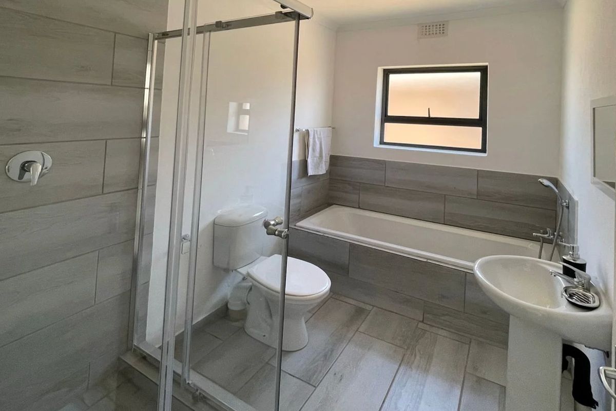 Modern bathroom featuring a glass shower enclosure, bathtub, pedestal basin, and toilet with neutral wood-look floor and wall tiling.