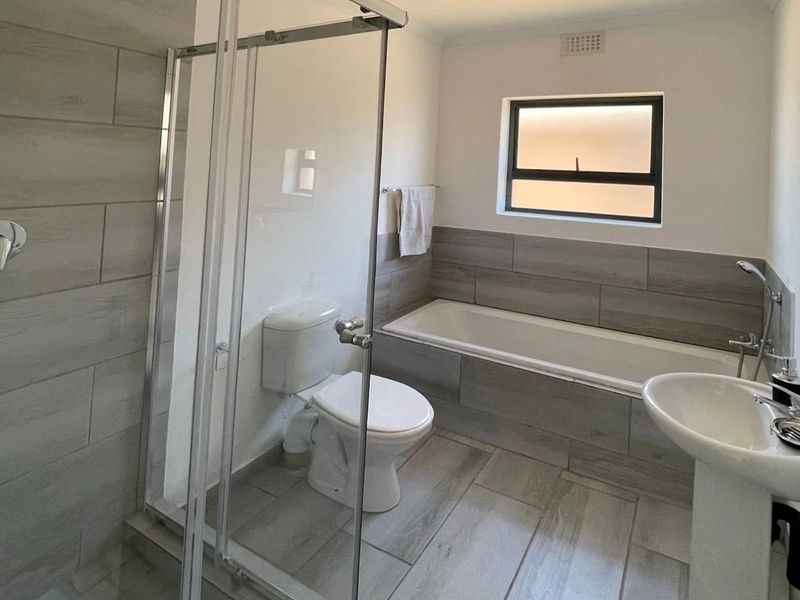 Modern bathroom featuring a glass shower enclosure, bathtub, pedestal basin, and toilet with neutral wood-look floor and wall tiling.