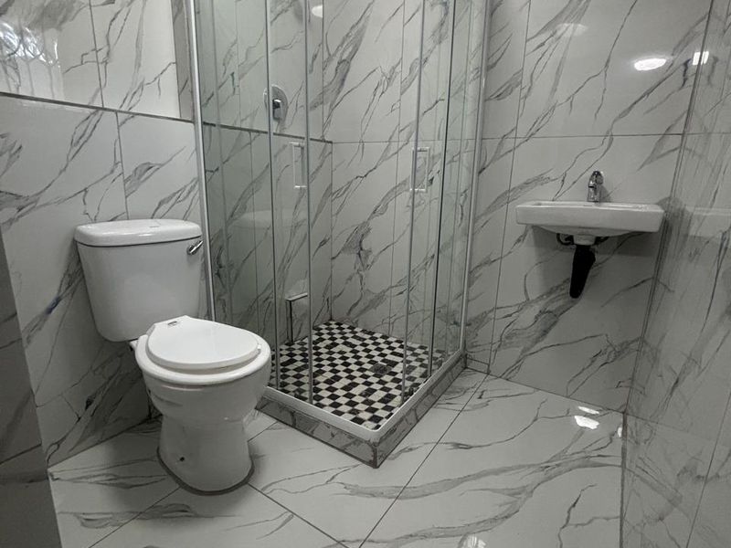 Modern bathroom featuring marble-look floor and wall tiles, a glass shower enclosure, a wall-mounted basin, and a standard toilet.