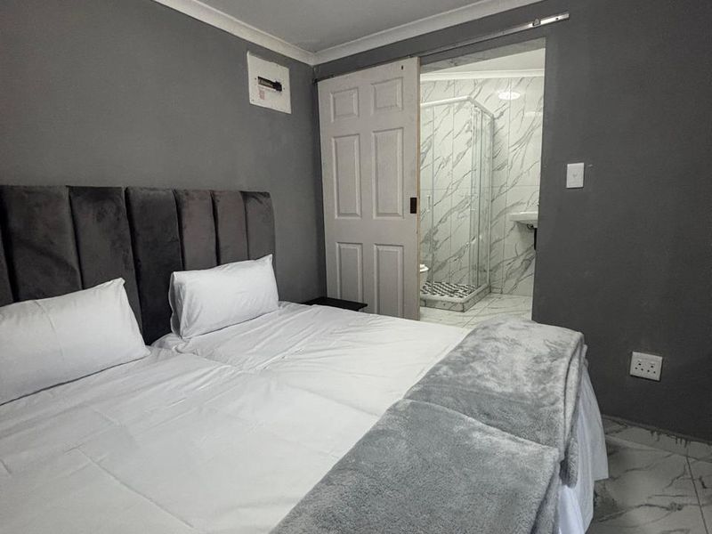 A modern bedroom featuring grey walls, marble-look floor tiles, and an en-suite bathroom with a glass-enclosed shower.