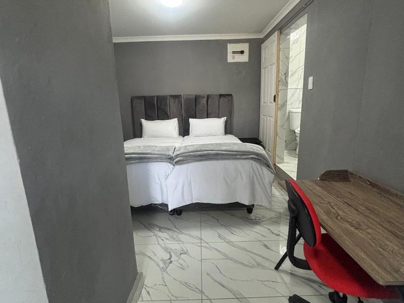 A bedroom featuring marble-look floor tiles, grey walls, and direct access to an en-suite bathroom.