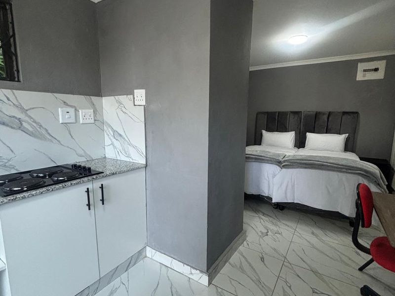 Modern open-plan studio apartment featuring a compact kitchen with marble-look finishes and a comfortable sleeping area with contemporary grey wall accents.