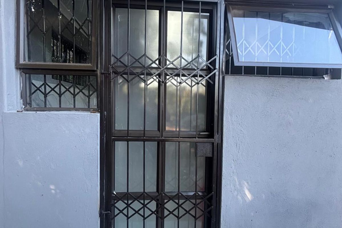 Exterior view of a rear entrance featuring a security gate, aluminium windows, and tiled patio flooring.