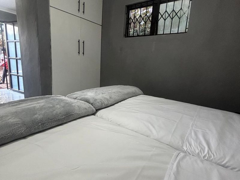 A bedroom featuring built-in cupboards, a window with security bars, and direct access to an outdoor area.