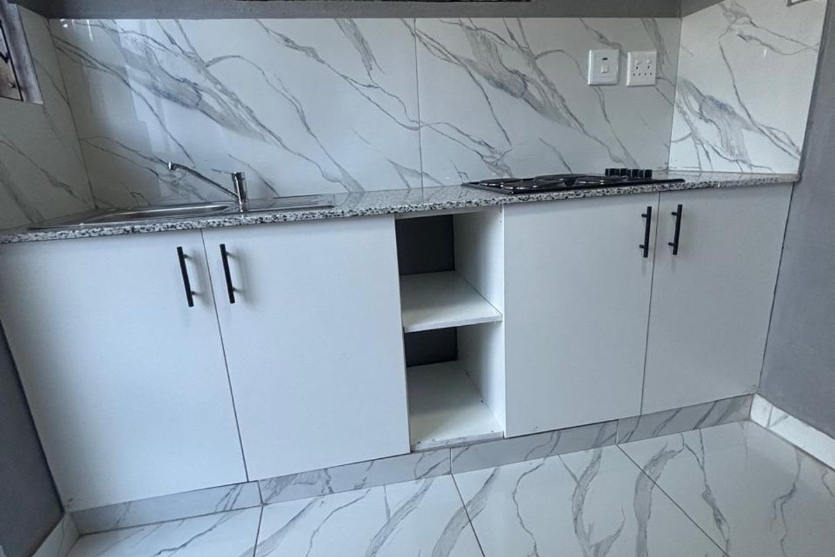 A modern kitchen featuring white cabinetry, granite countertops, a built-in hob, and marble-look tiled flooring and backsplash.