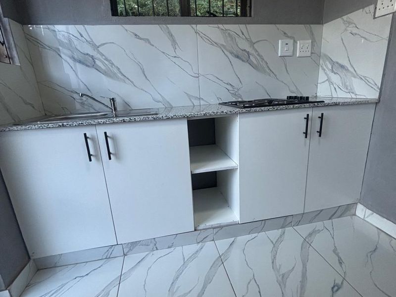 A modern kitchen featuring white cabinetry, granite countertops, a built-in hob, and marble-look tiled flooring and backsplash.