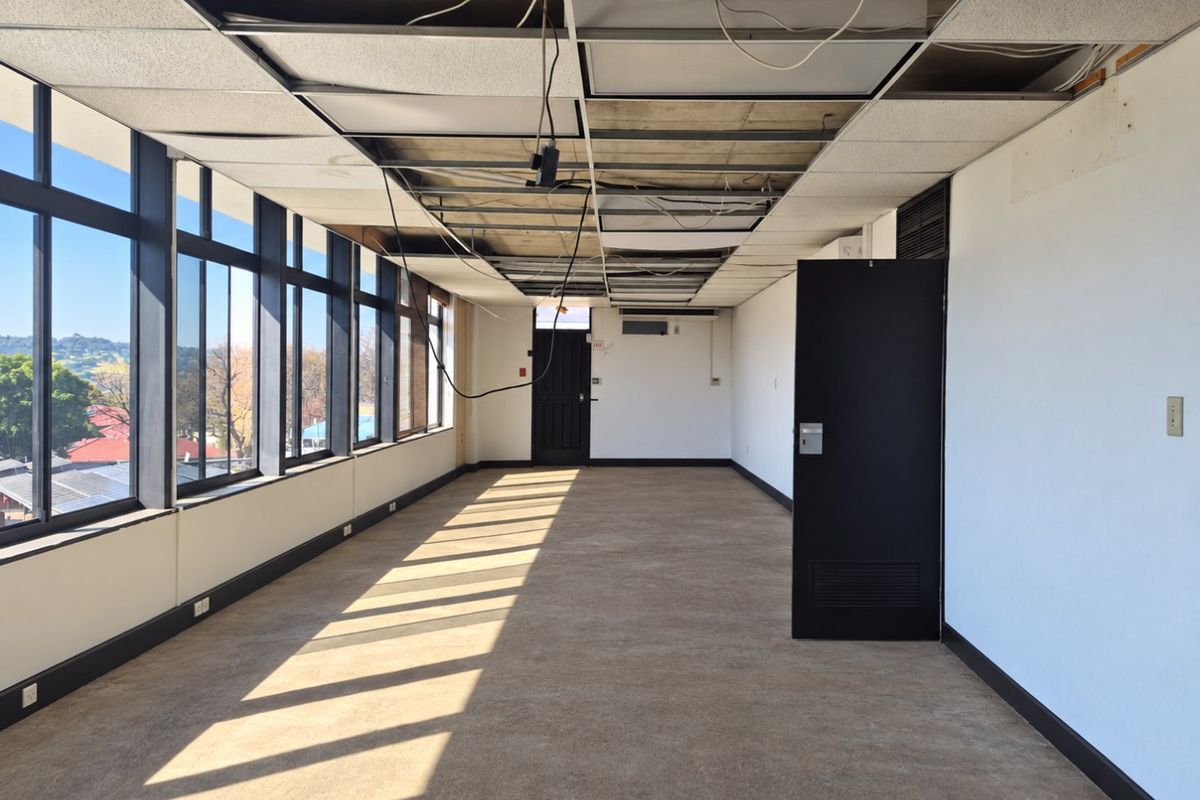 An empty commercial office space featuring large windows, carpeted flooring, and a suspended ceiling requiring repair and maintenance.