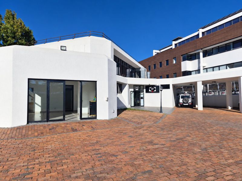 Front exterior view of a commercial building featuring a brick paved driveway, covered parking, and modern glass entrance doors.